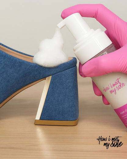 Person applying foam cleaner to a blue denim heel 