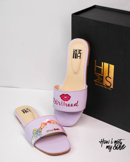 Pair of purple slides with floral design and 'Girlhood' text, next to a black box with 'HIMMS' branding.