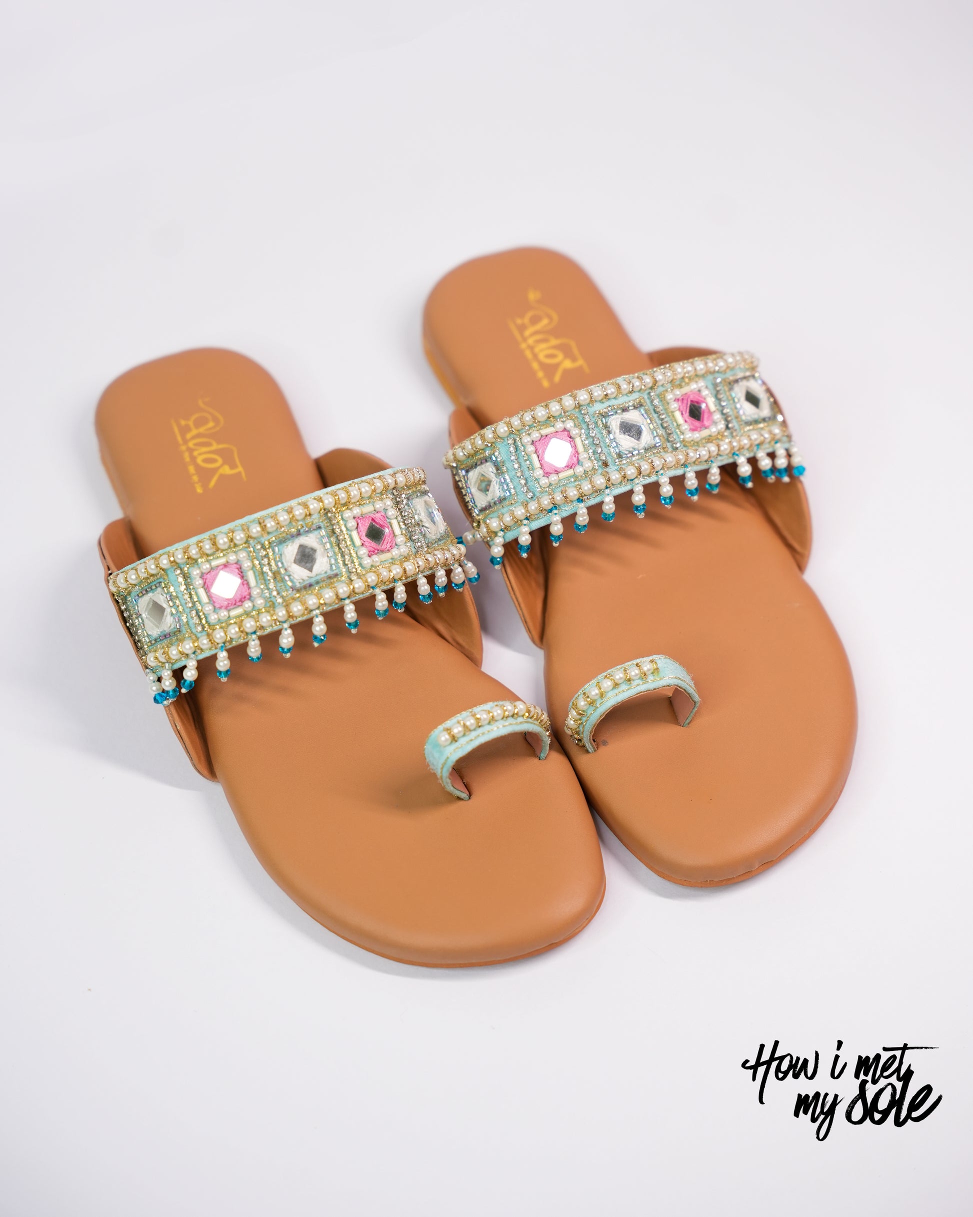 Pair of tan sandals with decorative multicolored straps on a white background