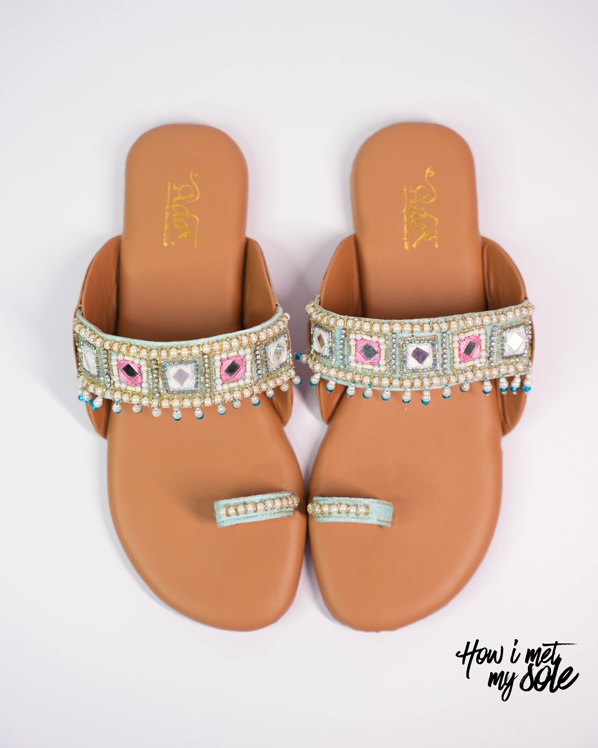 Pair of tan sandals with decorative straps on a white background