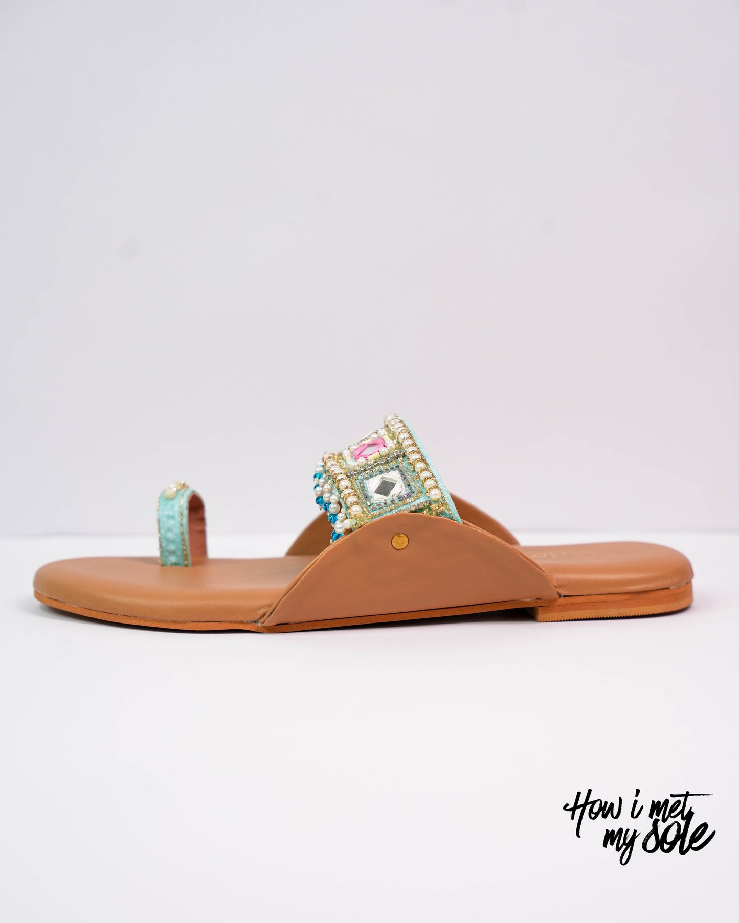 Tan sandal with decorative strap on a white background